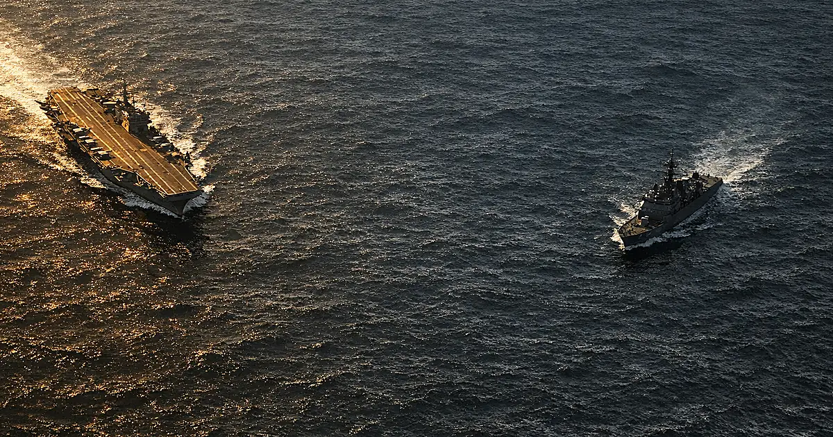 Aerial view of two naval vessels separated by dark ocean waters in contrasting light, depicting strategic standoff