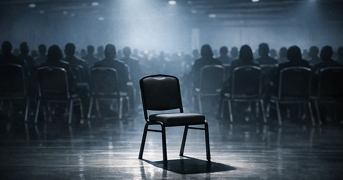 Empty chair spotlit in foreground of convention hall with silhouetted attendees in background
