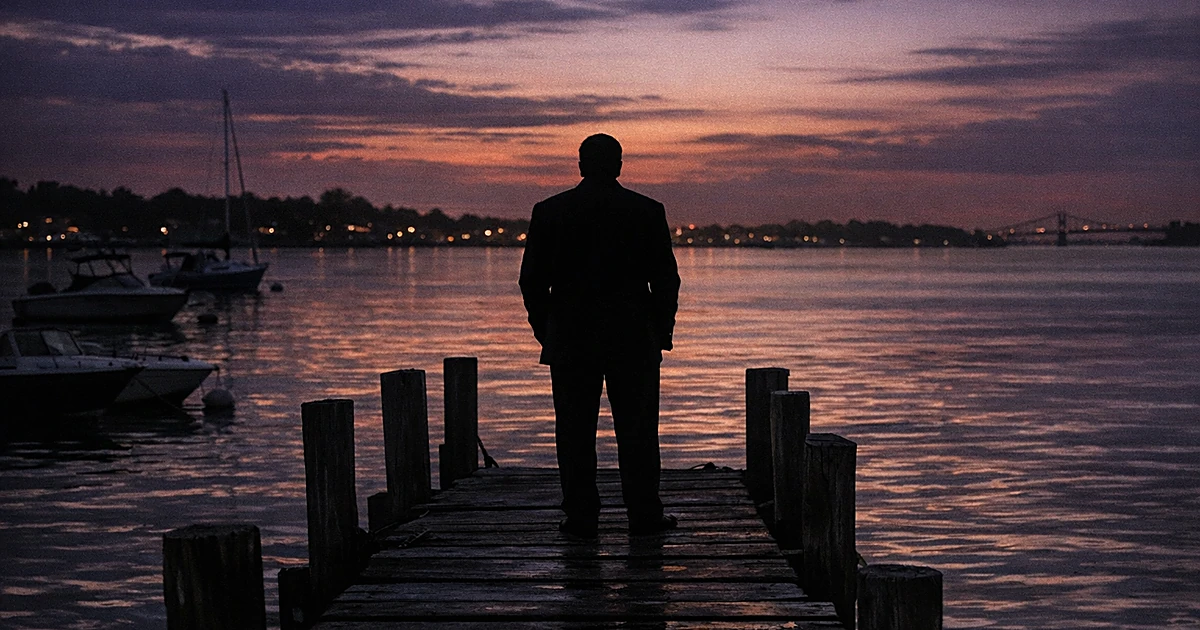 Silhouetted figure on City Island dock at dusk with boats and water reflecting twilight sky