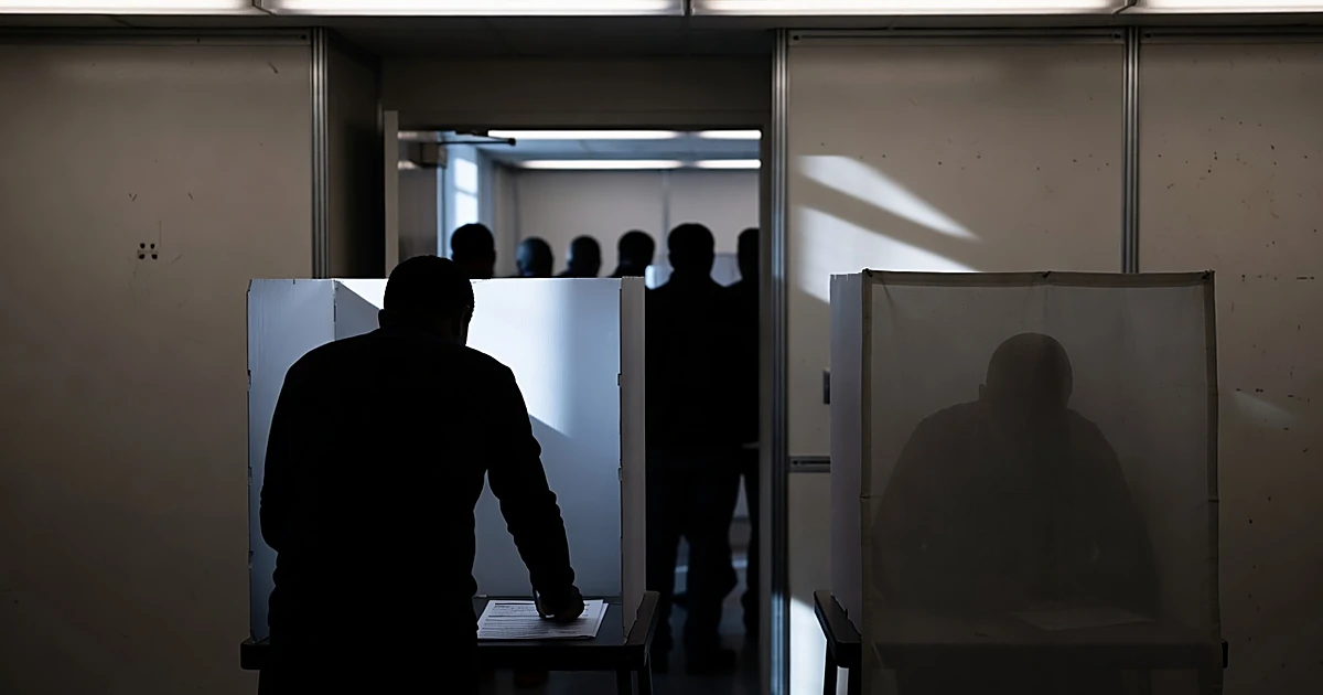 Silhouetted voters in polling booths during early voting, shown from behind with institutional lighting overhead