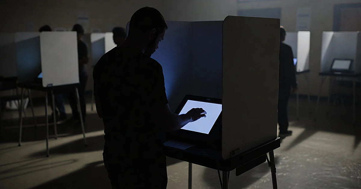 Silhouetted voter at illuminated touchscreen voting machine in darkened polling booth