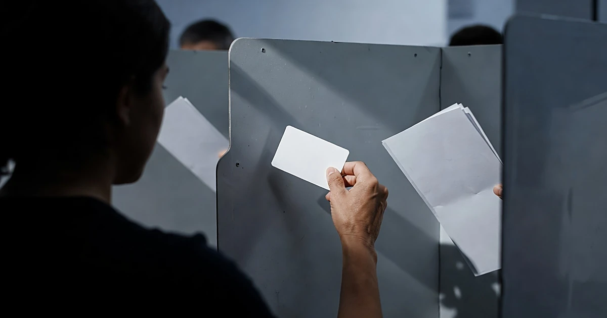 Hand placing blank student ID card on voting booth surface next to unmarked ballot paper
